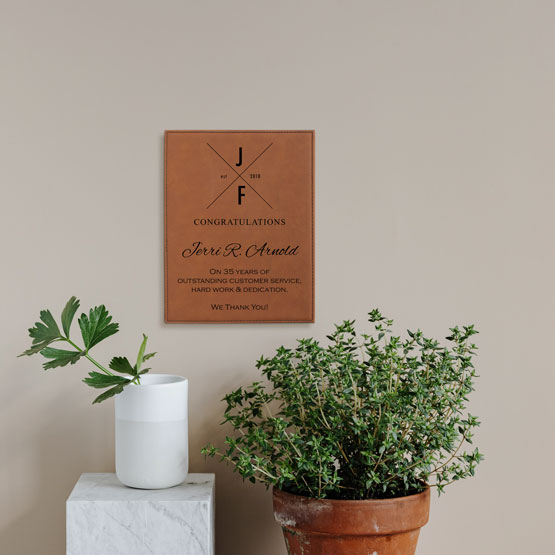 Rawhide Faux Leather Plaque With Logo And Years Of Service Congratulations Message On A Living Room Wall Above Plants