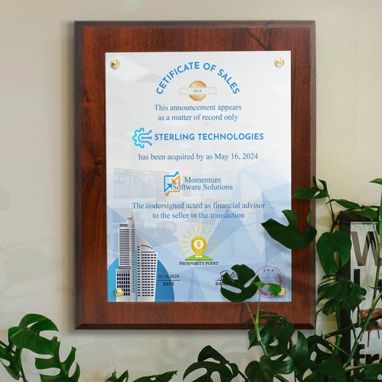 A framed ‘Certificate of Sales’ framed with a coated cherry board hanging on a beige wall, surrounded by green houseplants. The certificate features blue and gold text and graphics.