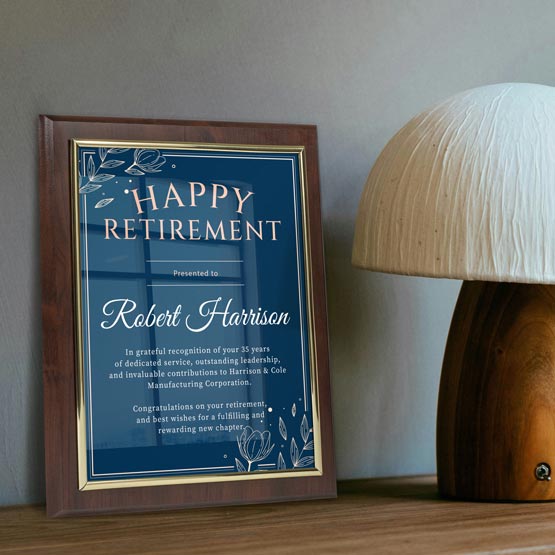 A framed retirement certificate leaning on a wooden surface next to a table lamp against a gray wall.