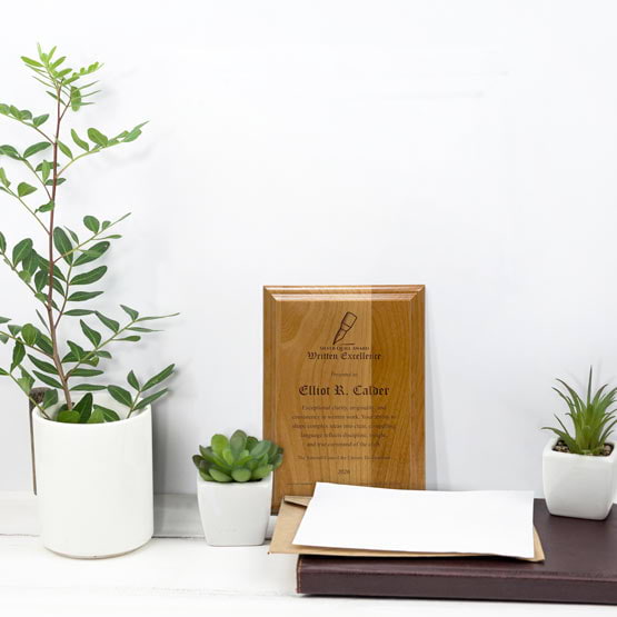 Solid Red Alder Wood Plaque Engraved With Award Message And Logo On A White Office Desk With Potted Plants And Notebook