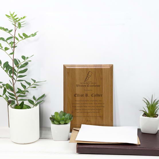 Solid Red Alder Wood Plaque Engraved With Award Message And Logo On A White Office Desk With Potted Plants And Notebook