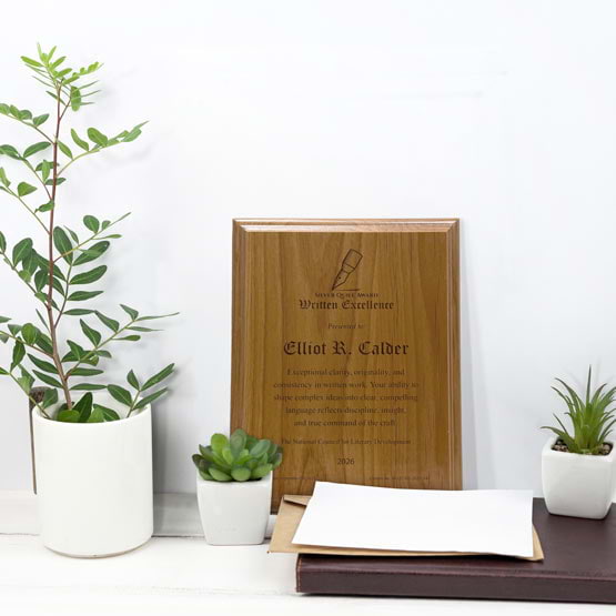 Solid Red Alder Wood Plaque Engraved With Award Message And Logo On A White Office Desk With Potted Plants And Notebook