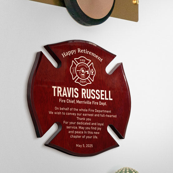 A personalized rosewood firefighter retirement plaque shaped like a Maltese cross, mounted on a white wall. The plaque as engraved beige text and a fire department emblem in the center.