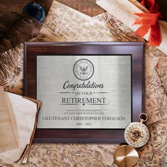 A retirement stainless steel plaque on a coated cherry board styled on a vintage map with old papers, a feather quill, a compass, and a red ribbon.
