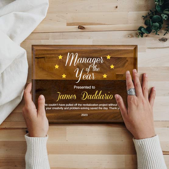 Woman Hands Holding Solid Walnut Plaque Award For Manager Of The Year With Name And Date And Message On A Wood Table
