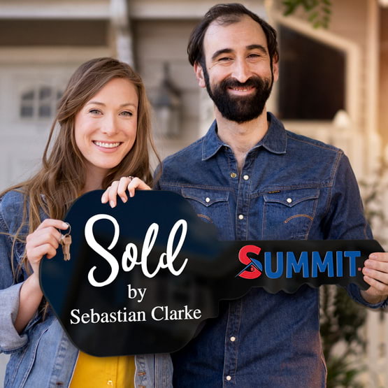 Happy Couple Outside Home Holding A House Key Shaped Black Acrylic Sign Printed With Sold By Message And Logo And Name