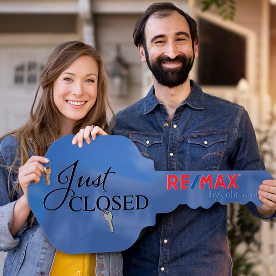 Happy Couple Outside Home Holding A House Key Shaped Blue Acrylic Sign Printed With Just Closed Message And Logo And Name