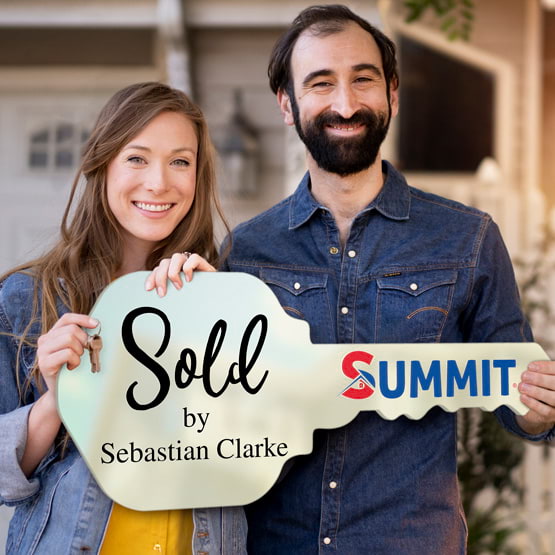 Happy Couple Outside Home Holding A House Key Shaped Ivory Acrylic Sign Printed With Sold By Message And Logo And Name