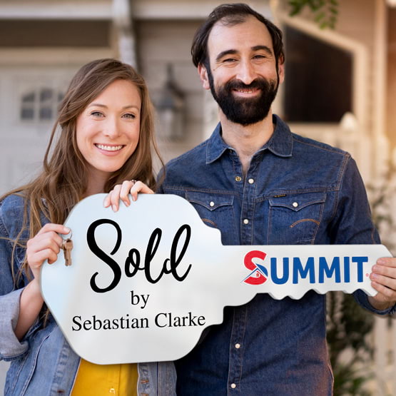 Happy Couple Outside Home Holding A House Key Shaped White Acrylic Sign Printed With Sold By Message And Logo And Name
