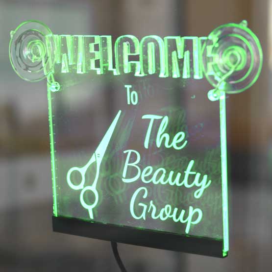 Green Edge Lit LED Acrylic Welcome Sign With Scissor Art And The Beauty Group Text Mounted Onto Glass Business Window