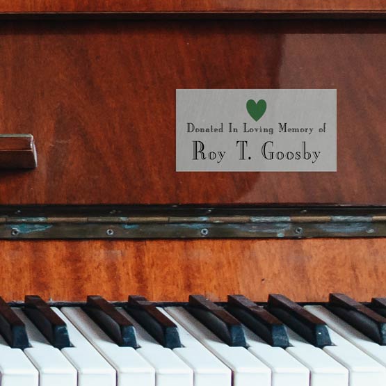 Custom Silver Aluminum Label Printed With Memorial Message And Name And Green Heart Mounted Onto Wood Piano Above Keys