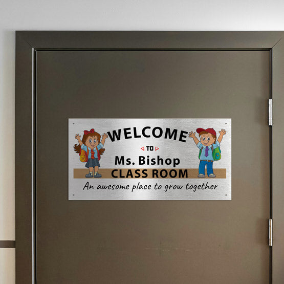 A silver metal sign with full color printing on a door. The sign is a welcome sign to Ms Bishop’s classroom attached to the door by four screws.