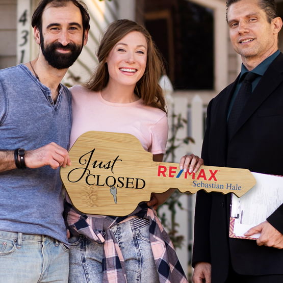 Realtor Posing Outdoors With Happy Couple Holding House Key Shaped Bamboo Sign Printed With Just Closed Message And Logo