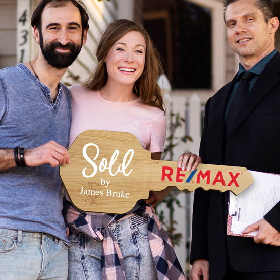 Realtor Posing Outdoors With Happy Couple Holding House Key Shaped Bamboo Sign Printed With Sold By Message And Logo
