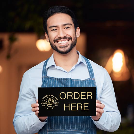 Happy Barista In Apron Outside Cafe Holding Custom Black And Gold Aluminum Sign Laser Engraved With Logo And Order Here Text