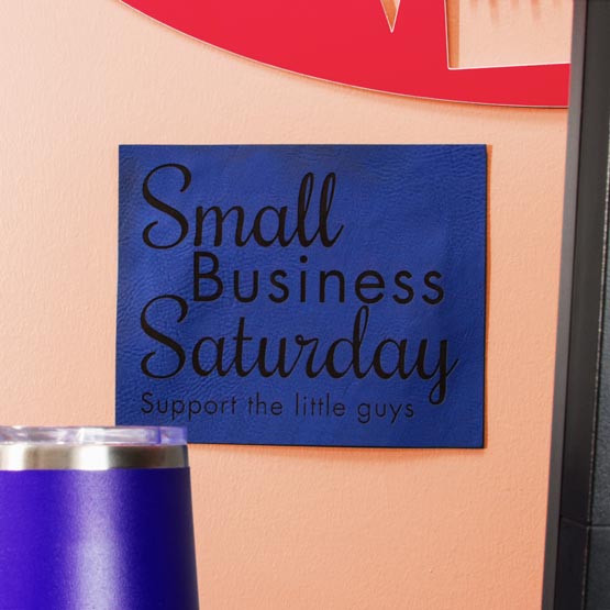 Blue And Black Faux Leather Sign Engraved With Small Business Saturday Message Mounted On Wall Near Door And Tumbler