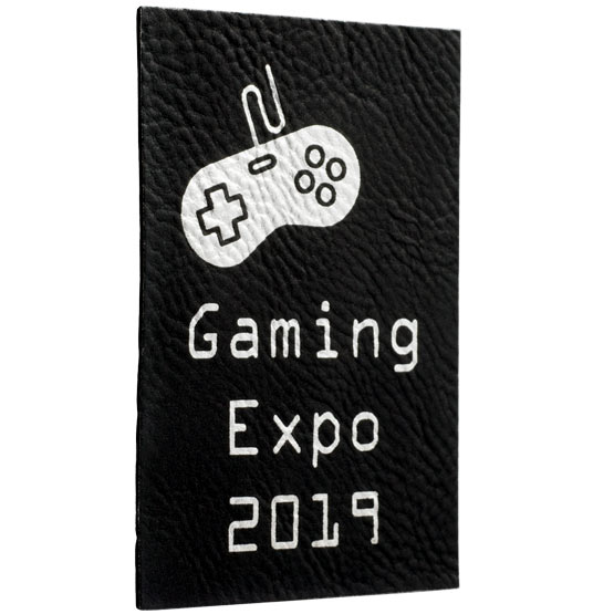Custom Black And Silver Faux Leather Label Engraved With Game Controller Art And Gaming Expo Text Against White Background