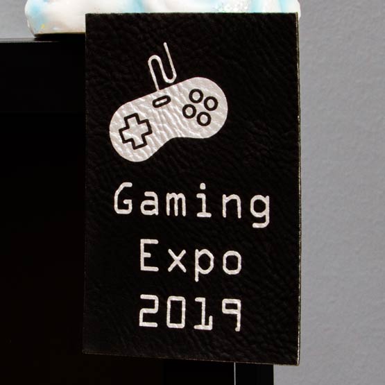 Black And Silver Faux Leather Label Engraved With Game Controller Art And Gaming Expo Text Mounted On Glass Business Window
