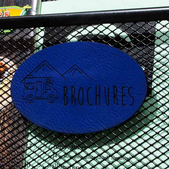 Custom Oval Blue And Black Faux Leather Label Engraved With Brochures Company Logo Mounted Onto Black Fence