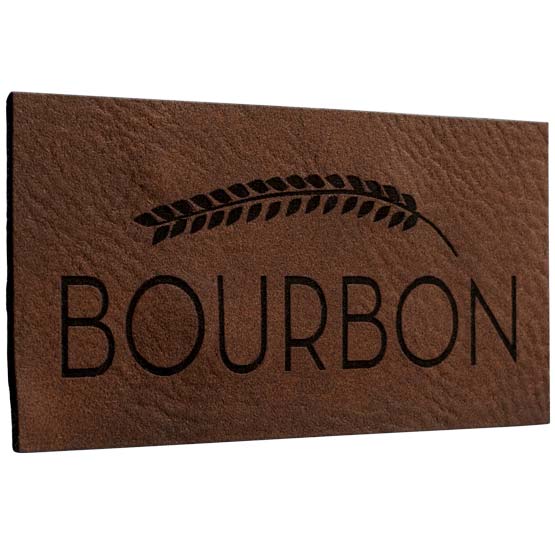 Custom Dark Brown And Black Faux Leather Label Engraved With Wheat Art And Bourbon Text Against White Background