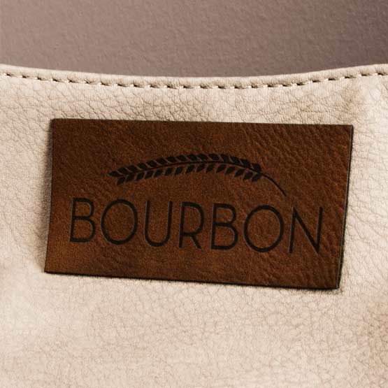 Dark Brown And Black Faux Leather Label Engraved With Wheat Art And Bourbon Text Fastened To White Faux Leather Sheet