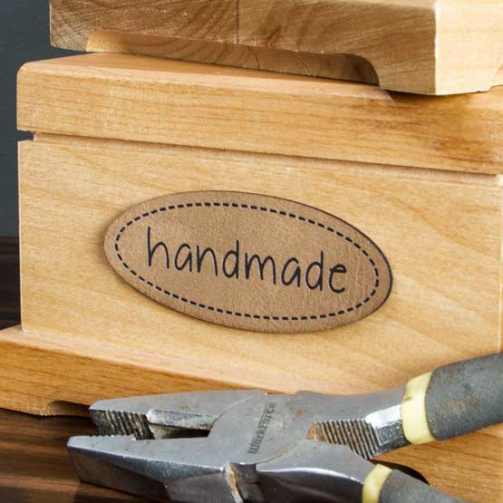 Light Brown And Black Faux Leather Label Engraved With Handmade Text And Stitching Art On A Wood Jewelry Box Near Pliers