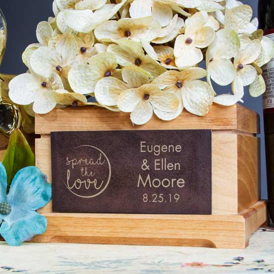 Rustic And Gold Faux Leather Label Engraved With Spread The Love Text And Couple Names And Date On Wood Planter With Flowers