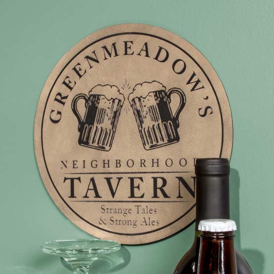 Light Brown And Black Faux Leather Sign Laser Engraved With Greenmeadows Tavern Logo And Slogan On Wall Near Beer Bottles