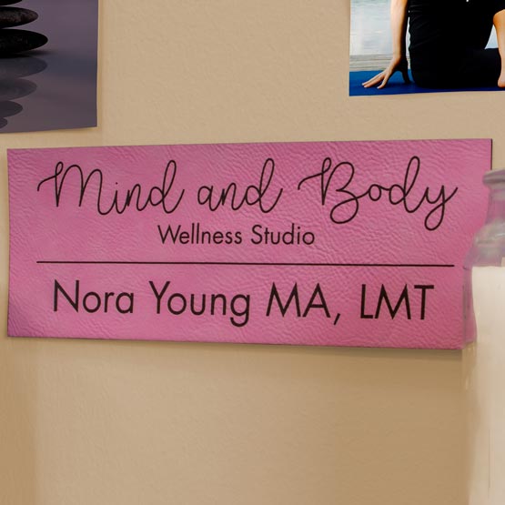 Pink And Black Faux Leather Sign Engraved With Mind And Body Wellness Studio Logo And Location Text On Wall With Photos