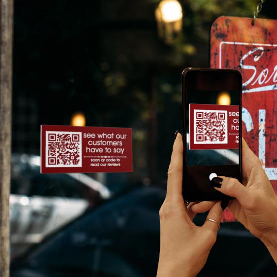 Woman Taking Phone Picture Of Red Plastic QR Tag Engraved With QR Code And See What Our Customers Say Message On Glass Window
