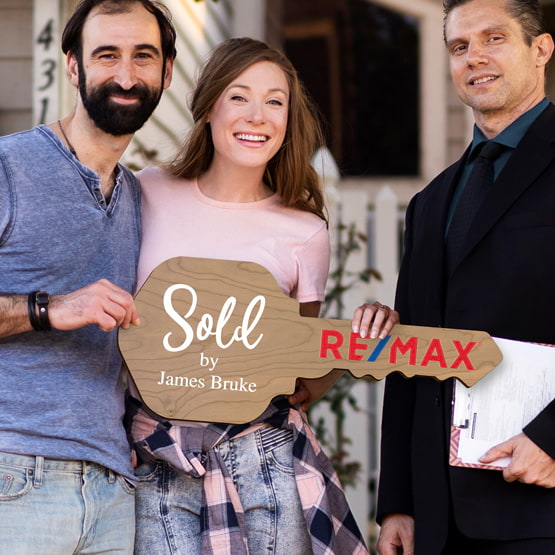 Realtor Posing Outdoors With Happy Couple Holding House Key Shaped Cherry Wood Sign Printed With Sold By Message And Logo