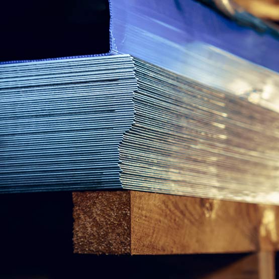 Close-up of a stack of stainless steel metal sheets on a wooden surface