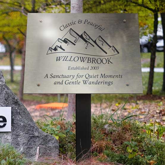 Stainless Steel Sign Laser Fused With Sample Willowbrook Logo And Text Displayed Outdoors Near Walking Path Via Sign Stand