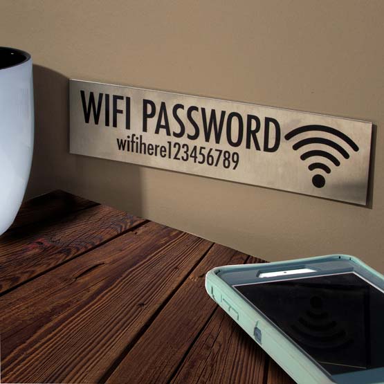 Eight By Two Stainless Steel WiFi Sign Laser Fused With WiFi Icon And Password On Wall Above Table With Coffee And Phone