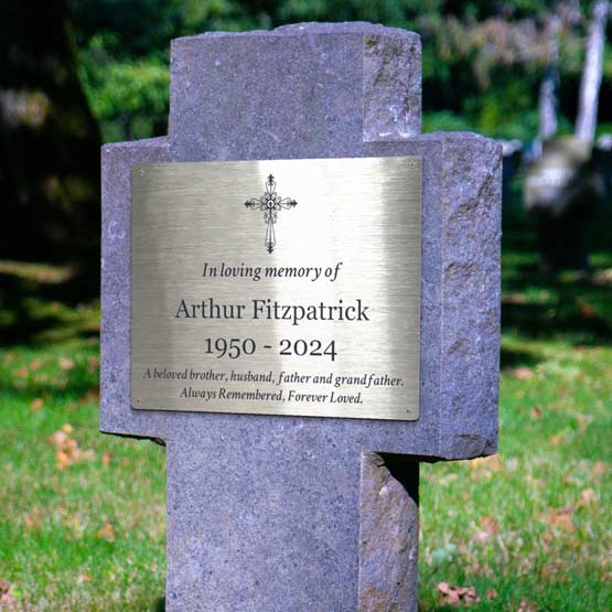 A gray stone cross grave maker with a stainless steel memorial sign reading a loving memorial tribute to Arthur Fitzpatrick with a cross clipart, photographed outdoors on grass.