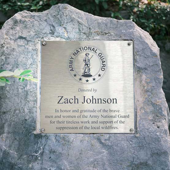 A stainless steel memorial plaque mounted on a large gray stone, featuring the Army National Guard emblem and the text 'Donated by Zach Johnson' with a memorial inscription for the Army National Guard.