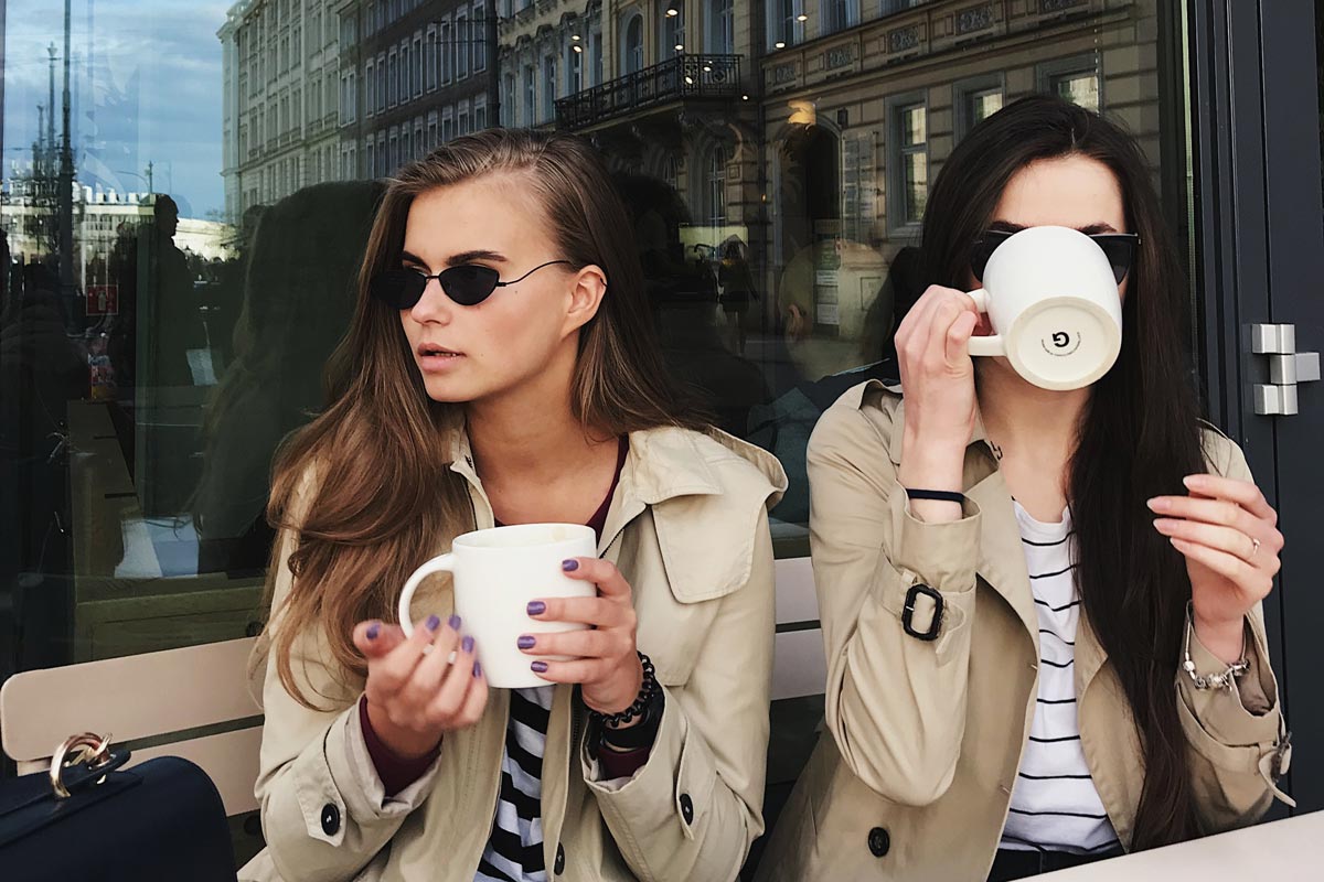 Two women sitting outside a cafe, drinking coffee.