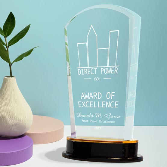 Acrylic award with gold mirror base on white desk with plant in a beige pear shaped pot.