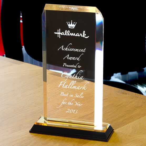 Acrylic award with clipped corners and gold mirror base on wooden computer desk in front of office chair.