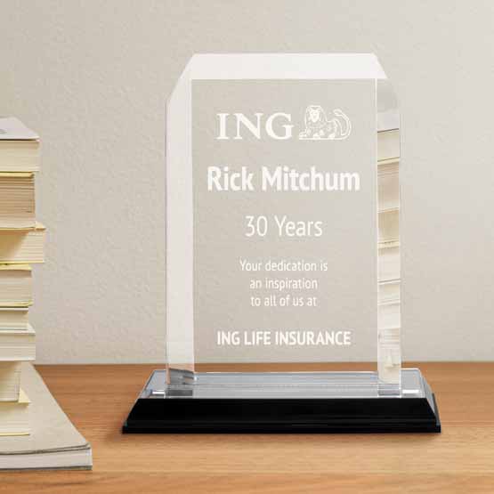 Acrylic award with clipped corners and silver mirror base on light wooden desk with stack of books.