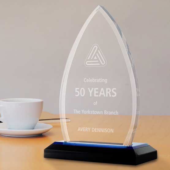 Engraved acrylic crest award with blue mirror base on table near white tea cup and saucer.