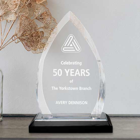 Custom engraved acrylic crest award on side table near vase of dried flowers.