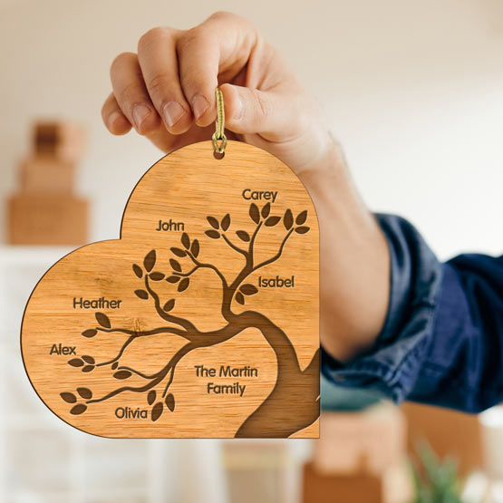 A laser cut bamboo Family tree ornament, cut into the shape of a heart. Ornament being held in a hand by a golden string.