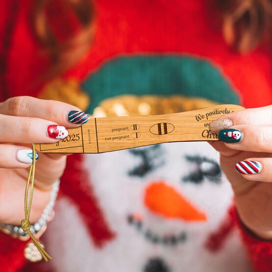 Woman In Snowman Christmas Sweater Holding Up Wood Ornament With Custom Pregnancy Test Design And Text