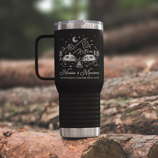 Custom Engraved 20 oz Black Tumbler on a wooden log with a sample engraving for Nicolas & Mariann