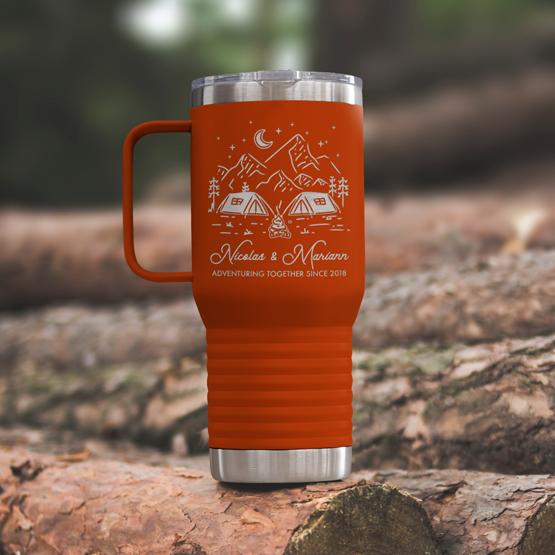 Custom Engraved 20 oz Orange Tumbler on a wooden log with a sample engraving for Nicolas & Mariann