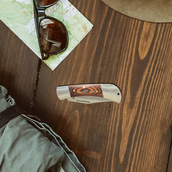 Custom Stainless Steel And Pakkawood Folding Knife Featuring Custom Summer Text And Sitting On Wood Table With Sunglasses