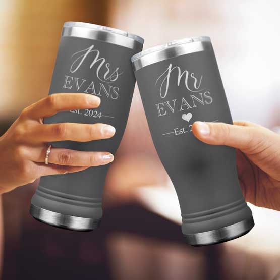 Two Custom Engraved Gray Beer Pilsner Tumblers held by woman and man with sample engraving for Mr & Mrs Evans