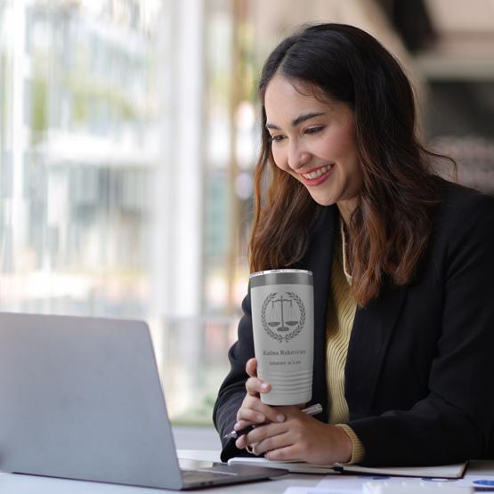 Custom White Scales of Justice Tumbler being held by a young lawyer working on a laptop. Engraved with your name and title.