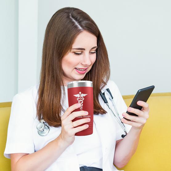 A medical professional holding a red tumbler that is personalized with their name and their title engraved on the front.